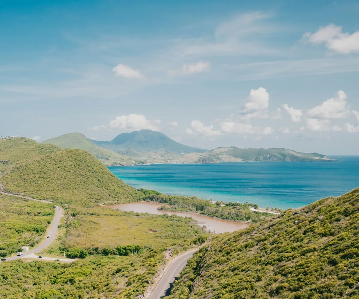 A coastal road through green hills with the sea and Nevis in the distance